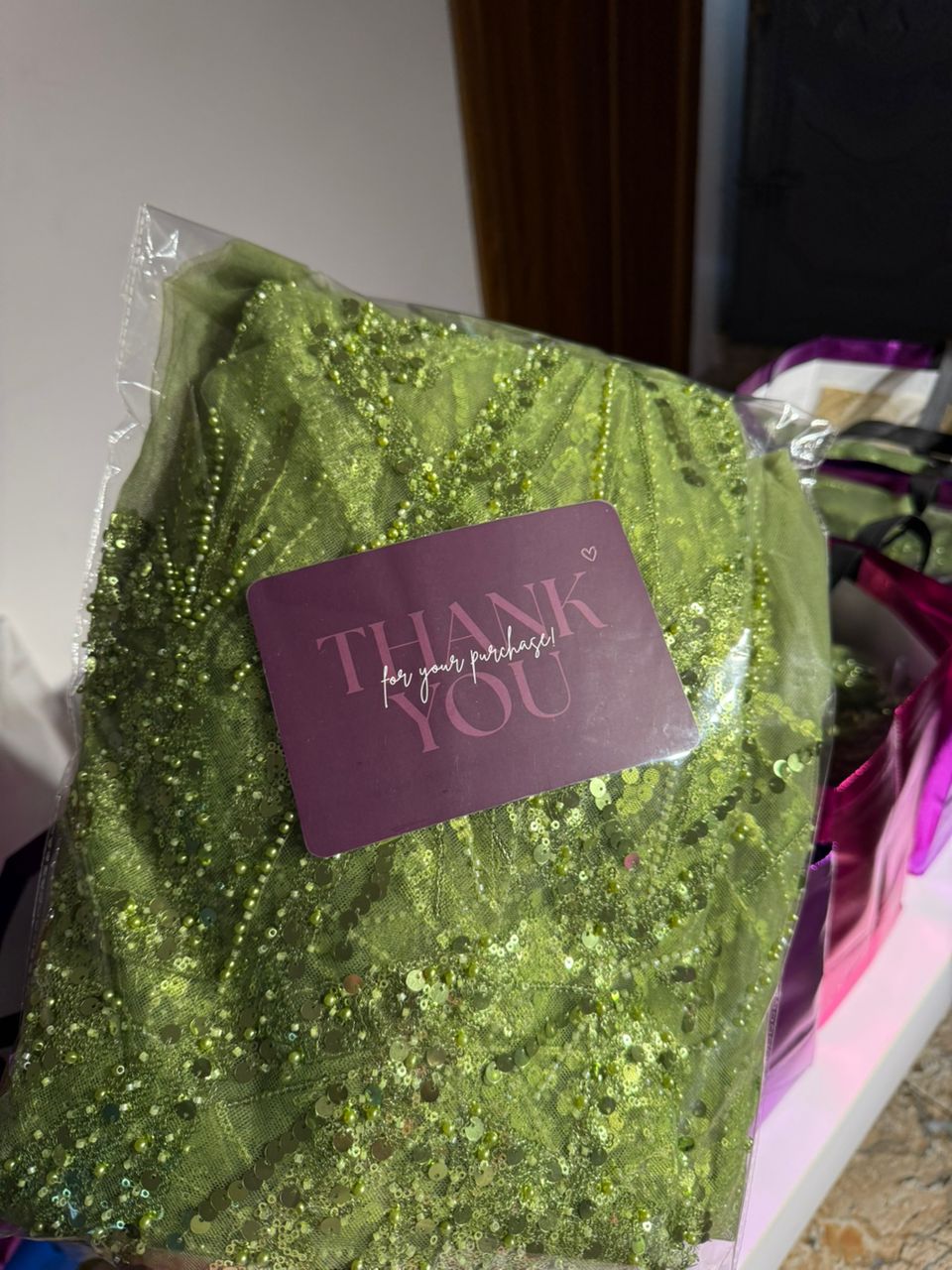 Close-up of emerald sequined asoebi fabric with a branded thank-you card